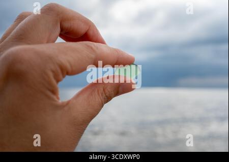 Gros plan avec mise au point sélective d'une main tenant un morceau de verre de mer vert clair givré. Banque D'Images