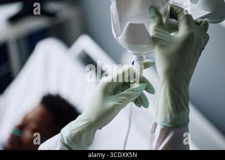 Infirmière méconnaissable portant des gants de protection en latex fixant une poche IV avec des liquides pour le patient dans le service hospitalier Banque D'Images