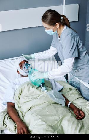 Vue verticale en grand angle d'une infirmière caucasienne portant un masque sur le visage en ventilation artificielle pour un jeune homme noir blessé Banque D'Images