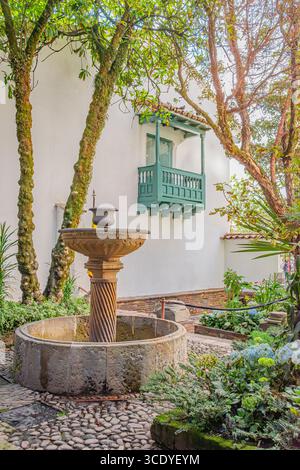 Un jardin pittoresque avec une fontaine en pierre entourée de verdure luxuriante à Bogotá, en Colombie. Un balcon traditionnel ajoute du charme à la scène. Banque D'Images