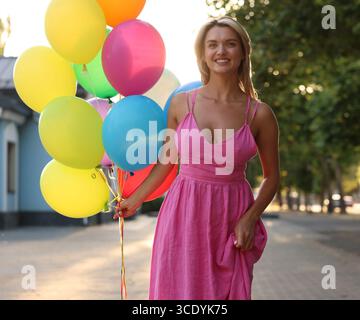 Femme souriante en robe avec un tas de ballons colorés à l'extérieur Banque D'Images