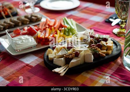 Un plat magnifiquement arrangé avec un assortiment de fromages, légumes frais et raisins. idéal pour les rassemblements ou les fêtes, cette configuration combine Banque D'Images