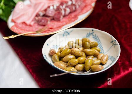 Un bol d'olives vertes et une assiette avec des charcuteries assorties, y compris du salami et du prosciutto, sont disposés sur une riche nappe rouge, créant une fea visuelle Banque D'Images