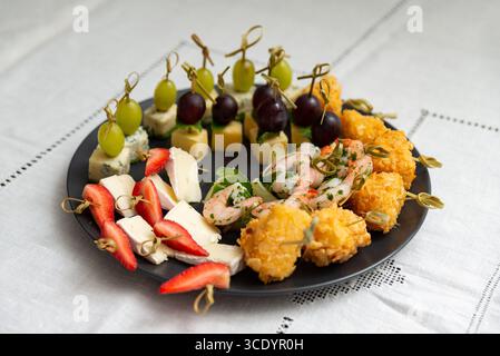 Un arrangement élégant de divers hors-d'œuvre sur une assiette noire, mettant en vedette des crevettes, des fromages et des fruits. parfait pour les fêtes et les rassemblements élégants, showca Banque D'Images