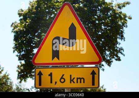 Panneau d'avertissement de la circulation indiquant route sinueuse pendant 1,6 kilomètres, situé dans un environnement rural avec ciel bleu clair et arbres verts en arrière-plan. Banque D'Images