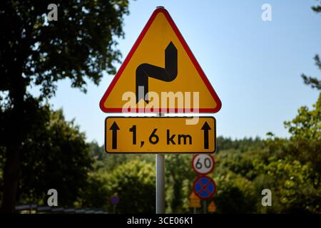 Panneau d'avertissement de la circulation indiquant route sinueuse pendant 1,6 kilomètres, situé dans un environnement rural avec ciel bleu clair et arbres verts en arrière-plan. Banque D'Images
