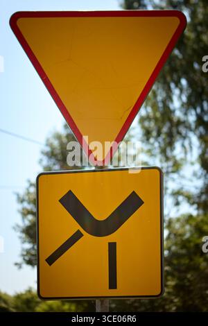 Un panneau de signalisation de rendement au-dessus d'un panneau jaune supplémentaire indiquant un carrefour latéral devant vous. Photographié à l'extérieur par une journée ensoleillée, rappelant aux conducteurs de le faire Banque D'Images