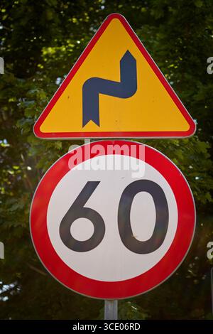 Panneau d'avertissement de la circulation indiquant la route sinueuse et la limite de vitesse de 60kmh, situé dans un environnement rural avec un ciel bleu clair et des arbres verts dans le backgrou Banque D'Images