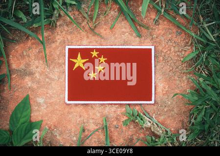 Drapeau chinois brodé sur une pierre rustique avec de l'herbe verte, symbolisant l'éco-tourisme, la sensibilisation à l'environnement et le changement climatique. Banque D'Images
