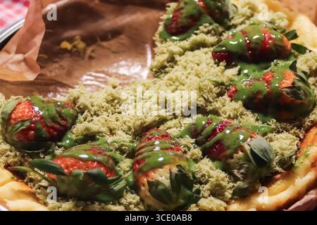 Dessert à la tarte aux fraises garni de matcha crémeux et de fromage au thé vert râpé, un mets de rue thaïlandais coloré dans un marché nocturne animé. Banque D'Images