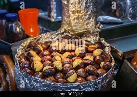 Un gros plan d'une casserole de châtaignes fraîchement grillées et craquelées en vente dans un chariot de cuisine de rue extérieur festif à Manhatten, New York City, États-Unis Banque D'Images