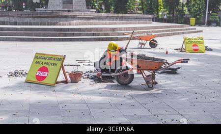 Un travailleur âgé répare des sols en pierre naturelle à Manahan, Surakarta, mettant en valeur les compétences traditionnelles et la précision dans les travaux de construction. Banque D'Images