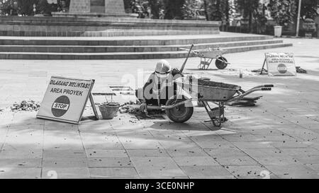 Un travailleur âgé répare des sols en pierre naturelle à Manahan, Surakarta, mettant en valeur les compétences traditionnelles et la précision dans les travaux de construction. Banque D'Images