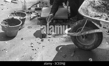 Un travailleur âgé répare des sols en pierre naturelle à Manahan, Surakarta, mettant en valeur les compétences traditionnelles et la précision dans les travaux de construction. Banque D'Images