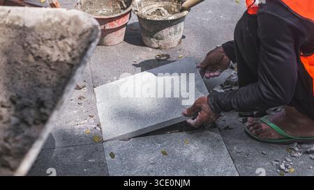 Un travailleur âgé répare des sols en pierre naturelle à Manahan, Surakarta, mettant en valeur les compétences traditionnelles et la précision dans les travaux de construction. Banque D'Images