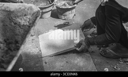 Un travailleur âgé répare des sols en pierre naturelle à Manahan, Surakarta, mettant en valeur les compétences traditionnelles et la précision dans les travaux de construction. Banque D'Images