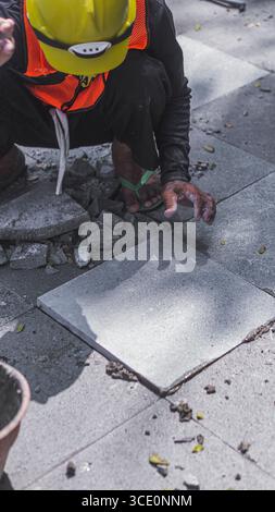 Un travailleur âgé répare des sols en pierre naturelle à Manahan, Surakarta, mettant en valeur les compétences traditionnelles et la précision dans les travaux de construction. Banque D'Images