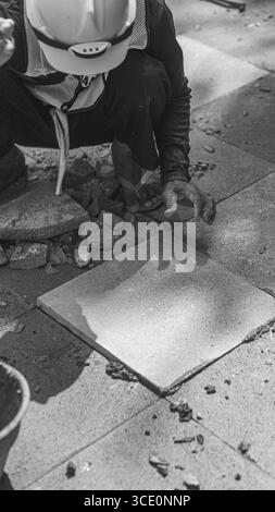 Un travailleur âgé répare des sols en pierre naturelle à Manahan, Surakarta, mettant en valeur les compétences traditionnelles et la précision dans les travaux de construction. Banque D'Images