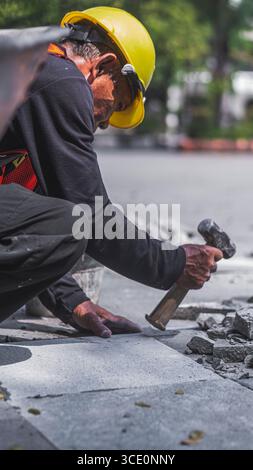 Un travailleur âgé répare des sols en pierre naturelle à Manahan, Surakarta, mettant en valeur les compétences traditionnelles et la précision dans les travaux de construction. Banque D'Images