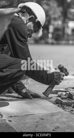 Un travailleur âgé répare des sols en pierre naturelle à Manahan, Surakarta, mettant en valeur les compétences traditionnelles et la précision dans les travaux de construction. Banque D'Images