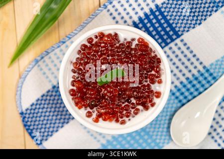Dessert sucré de perles de sagou rouge, ressemblant à des œufs de grenouille, servi avec des feuilles de pandan dans un bol en céramique Banque D'Images