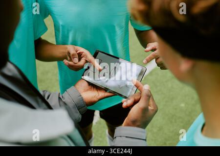 Adolescents multiethniques discutant de stratégie de jeu en utilisant la tablette numérique en extérieur Banque D'Images