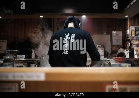 Le chef ramen japonais cuisine dans une cuisine traditionnelle de restaurant avec montée de vapeur, vue de derrière le comptoir au Japon Banque D'Images