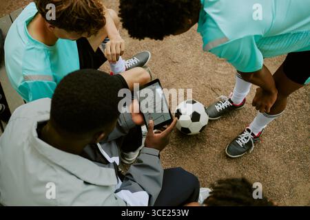 Adolescents multiethniques discutant de stratégie de football en utilisant la tablette numérique en extérieur Banque D'Images