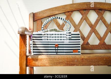 Sac à main en tissu rayé avec détail bouton sur un banc en bois à la lumière naturelle, style de vie minimaliste et accessoire de mode écologique. Banque D'Images