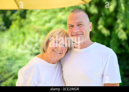 Portrait d'un couple aîné heureux embrassant dans un jardin verdoyant ensoleillé. Banque D'Images