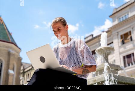 Jeune femme moderne utilisant son ordinateur portable à l'extérieur en ville Banque D'Images