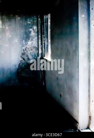 Une photo intérieure d'une pièce avec une fenêtre. Les murs sont un mélange de couleurs claires et sombres, et la pièce semble être dans un état de délabrement. Banque D'Images