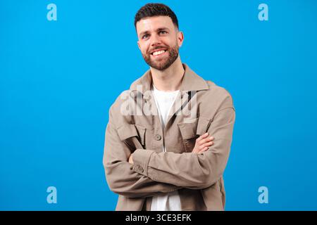 Homme souriant avec la barbe debout avec les bras croisés sur fond bleu Banque D'Images