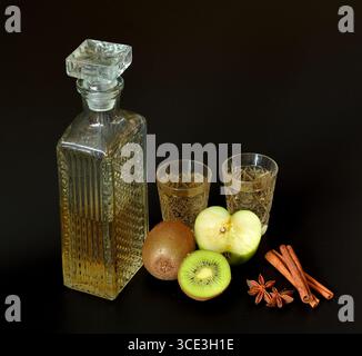 Kiwi maison et liqueur de pomme verte avec épices sur fond noir, fruits mûrs, cannelle et anis à proximité. Gros plan. Banque D'Images