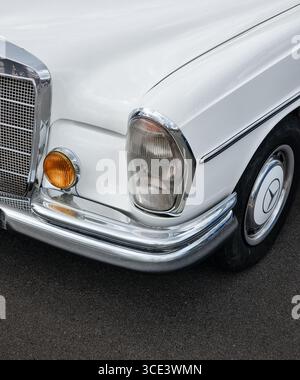 Coin avant gauche de la vieille Mercedes blanche des années 1960. Voiture classique dans le parking - vue rapprochée du phare, de la calandre, du phare antibrouillard, de l'aile, du capot de pare-chocs et de la roue. Banque D'Images