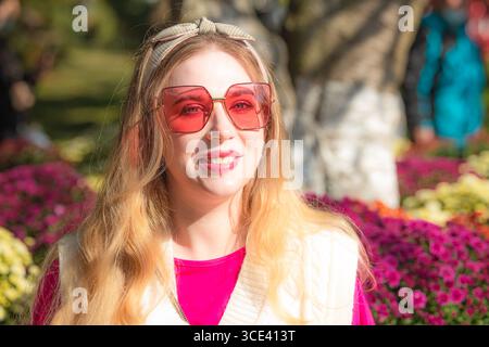 Une fille portant du rose avec des lunettes de soleil roses entourées de fleurs de chrysanthème. Banque D'Images