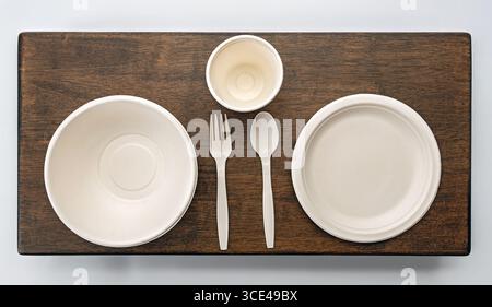 Un ensemble de vaisselle jetable écologique avec assiettes, bol, tasse, fourchette et cuillère sur une surface en bois, présentant des options de restauration durables Banque D'Images