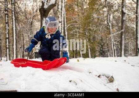 05.11.2016, Tartu, Estonie : enfant souriant tirant un traîneau rouge vers le haut de la côte un jour d'hiver enneigé. Banque D'Images