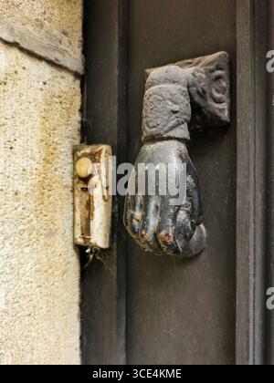 Un frappeur de porte en forme de main frappant est monté sur une entrée endommagée par les intempéries. A côté, une vieille sonnette ajoute du charme, la France Banque D'Images