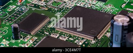 Aperçu détaillé d'une carte de circuit imprimé présentant des circuits intégrés, des condensateurs et des soudures complexes sur une surface verte. Banque D'Images