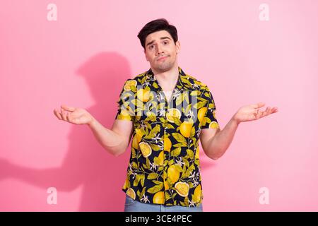 Jeune homme dans une chemise tropicale faisant des gestes avec une expression perplexe sur un fond rose Banque D'Images