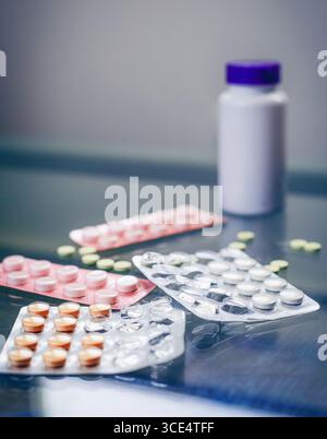 Une collection de blisters colorés se trouve dispersée sur une surface réfléchissante, accompagnée d'une bouteille blanche avec un bouchon violet. Diverses pilules sont visi Banque D'Images