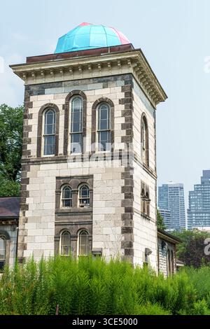 Un grand bâtiment en pierre avec des fenêtres cintrées et un toit en dôme bleu et rose s'élève au-dessus du feuillage vert Banque D'Images