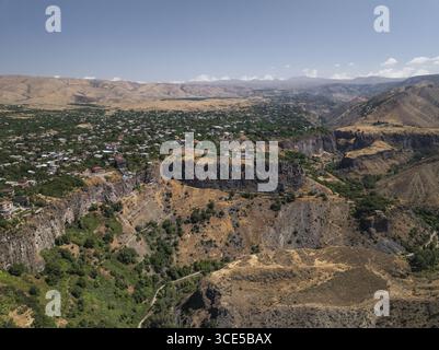 Vue aérienne d'un canyon profond, une ville nichée au loin, et le terrain accidenté, Garni, province de Kotayk, Arménie. Banque D'Images