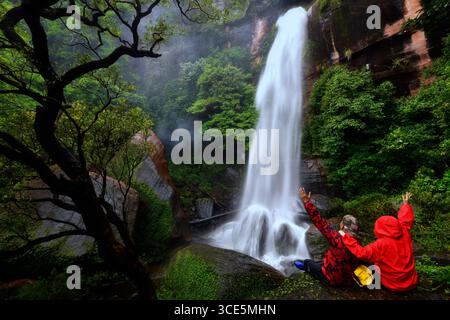 Vue arrière de deux personnes assises près de la cascade de Tad Wimanthip, parc national de Phulungka, province de Bueng Kan, Thaïlande Banque D'Images