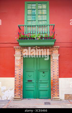 Une porte verte vibrante avec un balcon orné de fleurs contre un mur rouge à Bogotá, en Colombie, mettant en valeur des détails architecturaux colorés. Banque D'Images