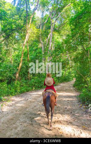 Une scène sereine d'une femme chevauchant un cheval le long d'un chemin sablonneux dans la verdure luxuriante du parc Tayrona, Santa Marta, Colombie. Banque D'Images
