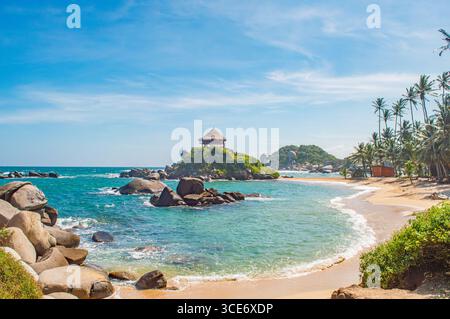Vue imprenable sur la plage dans Tayrona Park, Santa Marta, avec des eaux turquoises, des paysages rocheux et des palmiers sous un ciel bleu clair. Banque D'Images