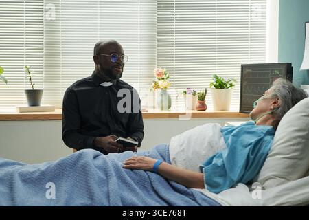 Aumônier noir d'âge moyen réconfortant une femme caucasienne senior à l'hôpital Banque D'Images