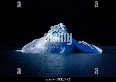 L'iceberg bleu flotte sur les eaux profondes du fjord de Dickson, dans le parc national du nord-est du Groenland. Fond sombre avec reflet montrant dans le ripp doux Banque D'Images